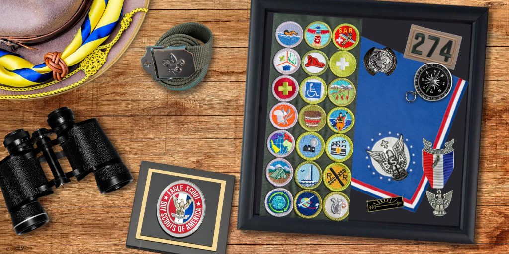 Eagle scouts shadow box filled with memorabilia and scouting america paperweight on desk by binoculars