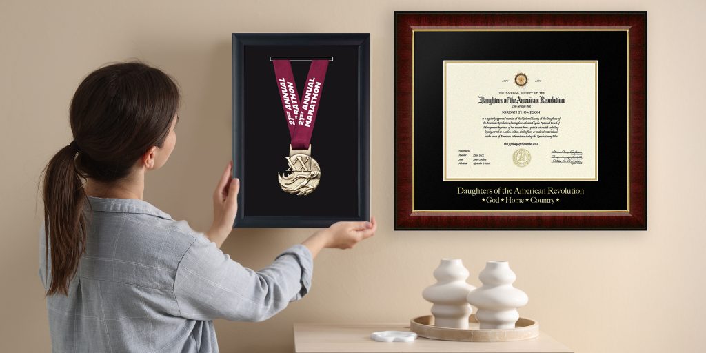 woman hanging marathon medal shadow box and custom certificate frame on wall