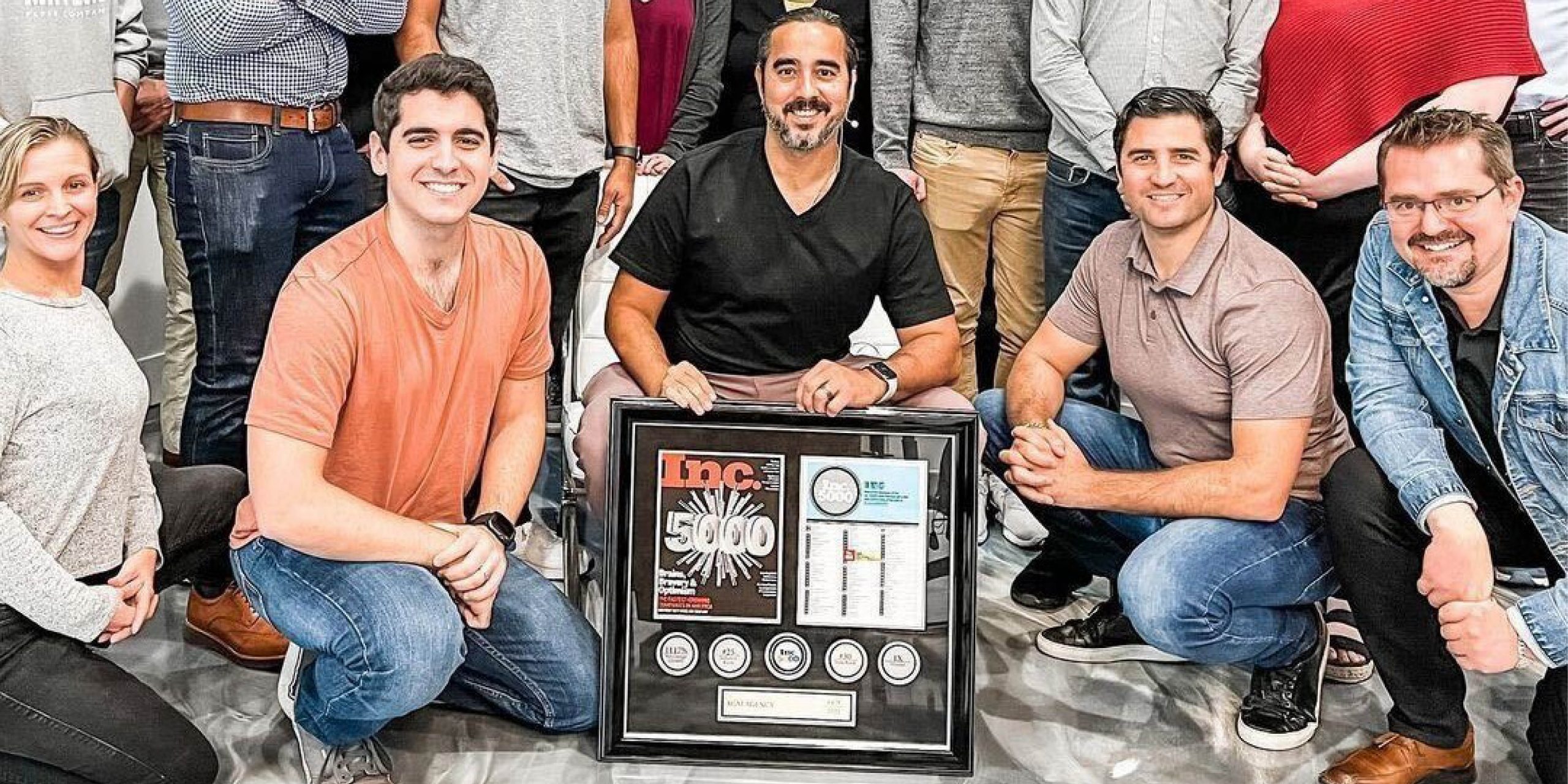 group of employees smiling in front of a custom INC 5000 medallion plaque and frame