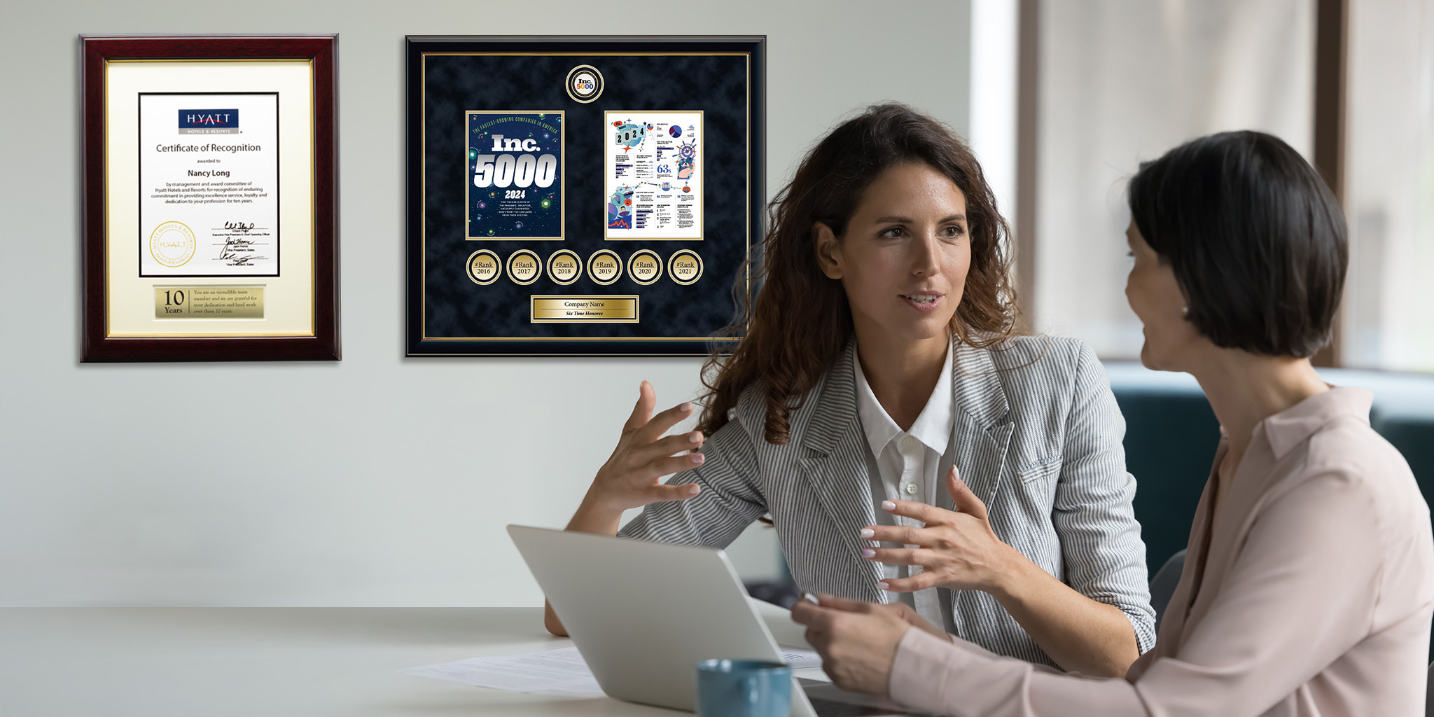 boss talking to employee in office with custom award and certificate frames on wall in background