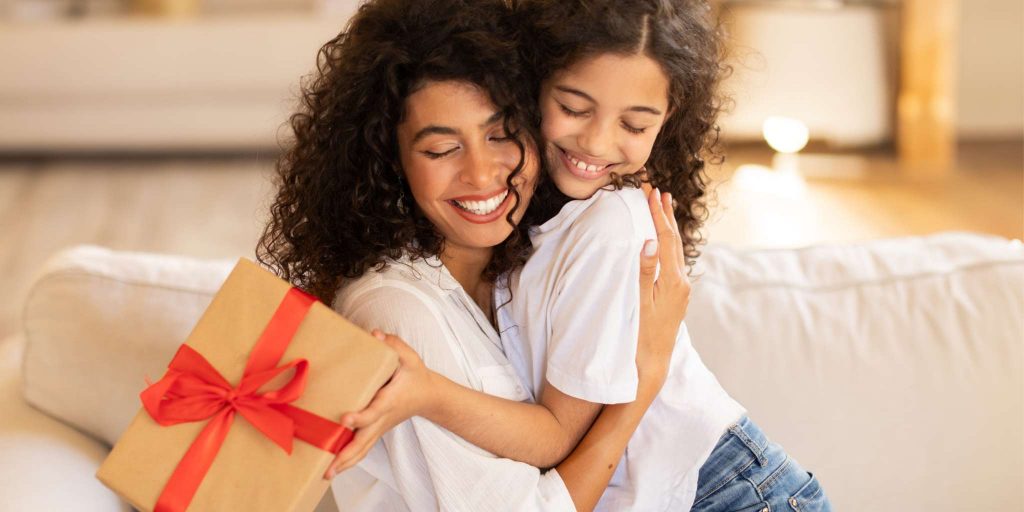 daughter handing a mother's day gift and mom smiling and hugging her daughter