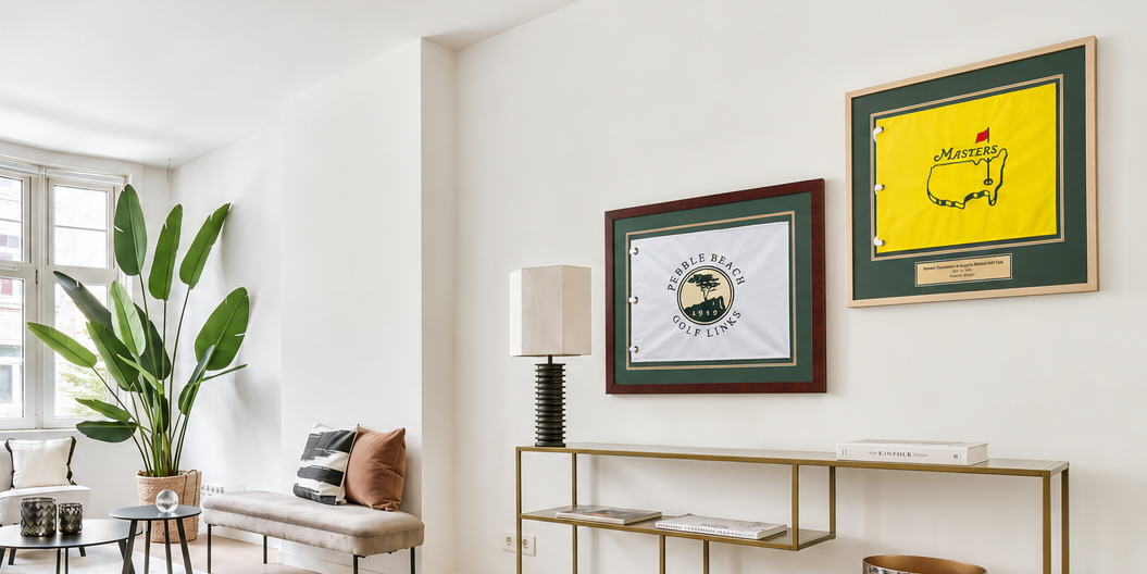 Bright and modern living room with white walls and plants featuring two golf flag frames on the wall side by side over a modern table with a lamp on it.